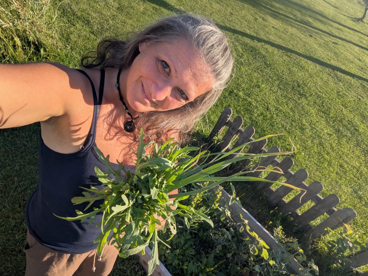 Frau mit langen Haaren hält frische Kräuter im Garten.